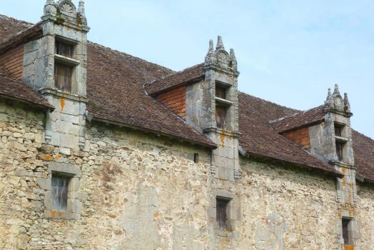 Une maison ancienne en pierre avec des fenêtres sur le toits.