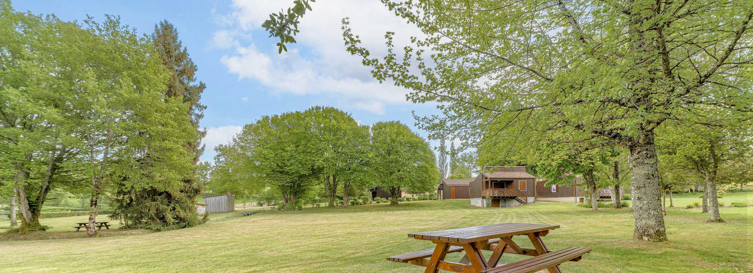 Le parc du hameau des gîtes avec vu sur les chalets et un banc.